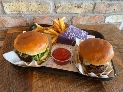 A tray with two burgers, lettuce, and a side of fries and ketchup on a wooden table.