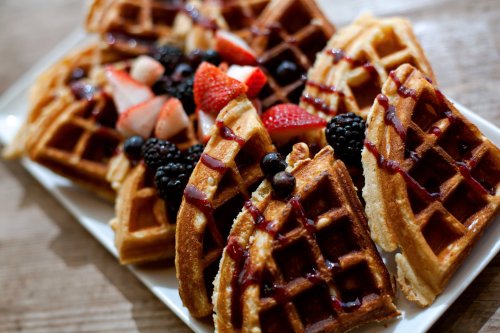 A plate of golden waffles topped with strawberries, blackberries, blueberries, and drizzled with syrup.