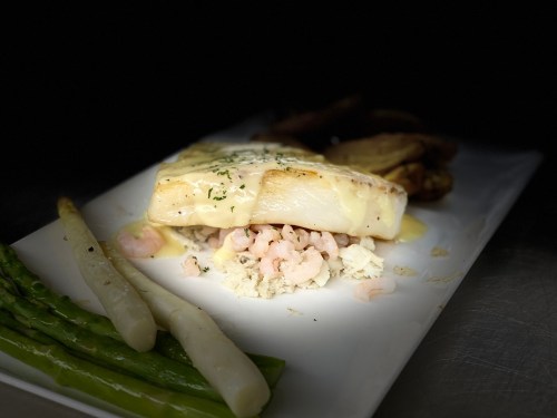 A plated dish featuring fish on a bed of shrimp and crab, accompanied by asparagus and potatoes.