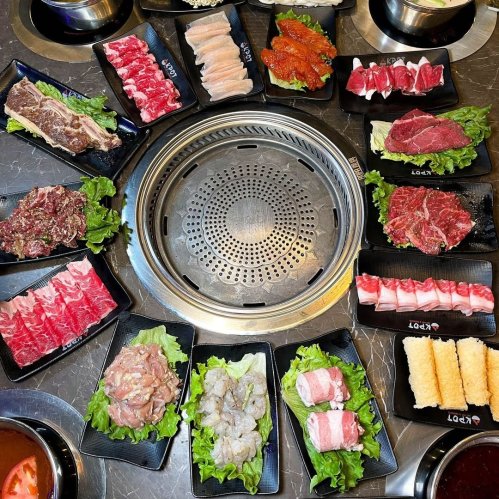 A variety of raw meats and seafood arranged on plates with lettuce, surrounding a grill in the center.
