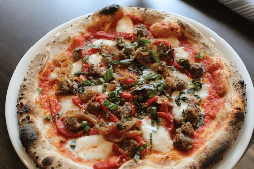 A freshly baked pizza topped with mozzarella, sausage, red peppers, and fresh basil on a golden crust.
