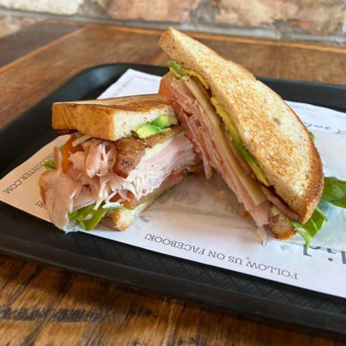 A sandwich with layers of turkey, ham, lettuce, and tomato on whole grain bread, served on a tray.