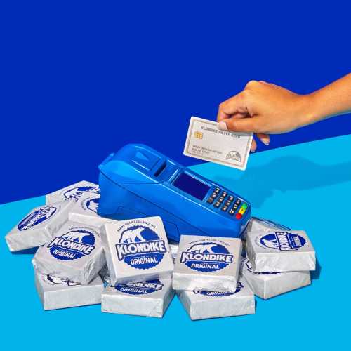 A hand holds a card above a blue payment terminal surrounded by Klondike ice cream bars on a colorful background.