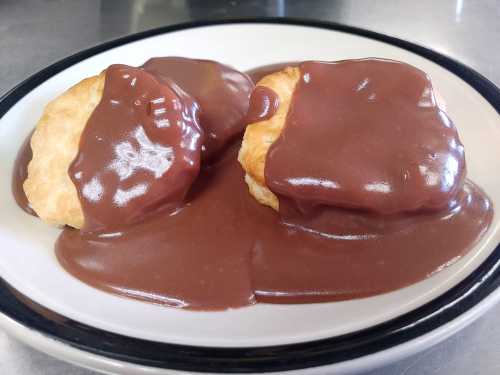 Two flaky biscuits topped with a rich, glossy chocolate sauce on a white plate.