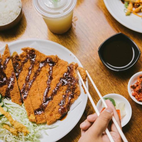 A plate of sliced fried chicken with sauce, served with salad, rice, and dipping sauce, alongside a drink.