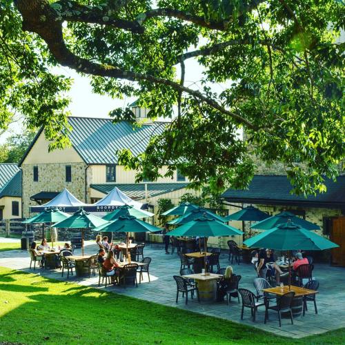 Outdoor dining area with green umbrellas, tables, and people enjoying a sunny day near a stone building.
