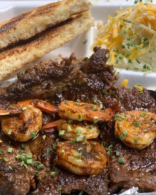 A plate featuring grilled shrimp and steak, served with toasted bread and a side of shredded cheese and salad.