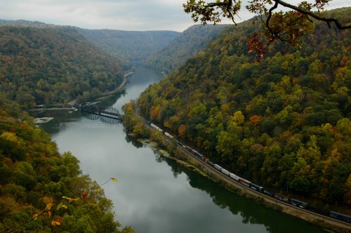 A scenic view of a river winding through lush, green hills with a train traveling along the water's edge.