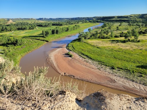 A winding river flows through lush green fields and hills under a clear blue sky.