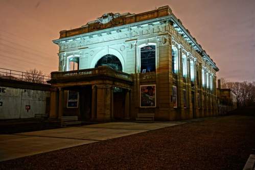 Historic building illuminated at night, showcasing architectural details against a cloudy sky.