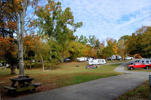 A scenic campground with colorful autumn trees, parked RVs, and a picnic area on a sunny day.