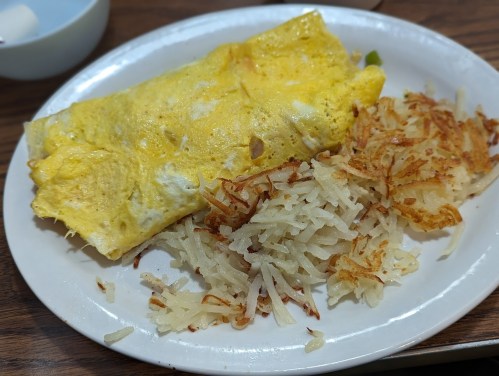 A plate with a fluffy omelet and crispy hash browns, served on a wooden table.