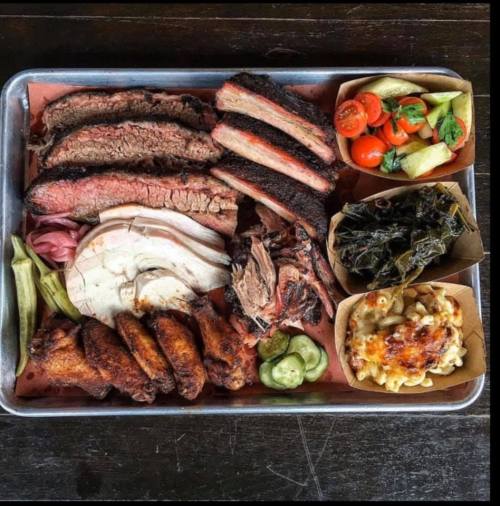 A platter of assorted meats including brisket, ribs, and chicken, accompanied by sides of vegetables and macaroni.