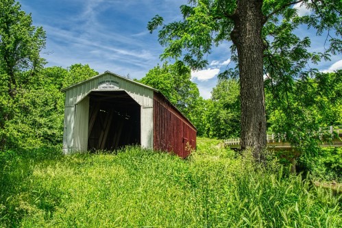 A red and white covered bridge surrounded by lush green grass and trees under a clear blue sky.