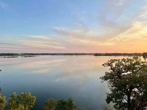 A serene lake at sunset, reflecting colorful skies and surrounded by trees.
