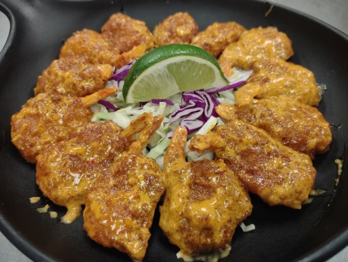 A skillet of spicy shrimp topped with a lime wedge and served on a bed of shredded cabbage and purple cabbage.