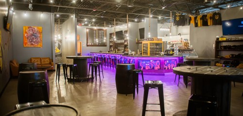 A modern bar interior with colorful lighting, high tables, and a long counter, creating a vibrant atmosphere.