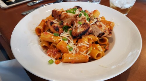 A plate of rigatoni pasta topped with grilled chicken, cheese, and green onions in a rich tomato sauce.
