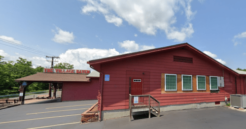 A red wooden building with a sign reading "The Wildlife Haven," surrounded by a parking lot and blue sky.