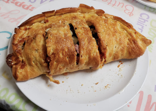 A golden-brown, sliced pastry filled with ham, cheese, and vegetables on a white plate.