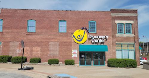 Exterior of the Discovery Center building, featuring a large logo and blue windows, set against a clear sky.