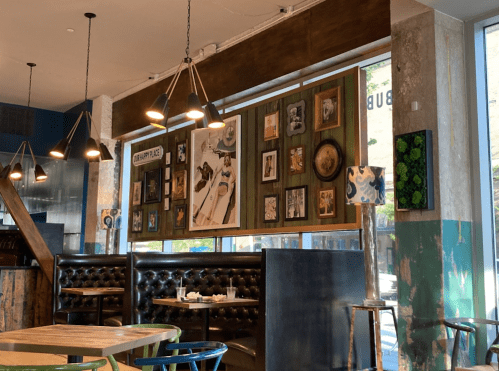 A cozy restaurant interior featuring wooden tables, black leather seating, and a gallery wall of framed art.
