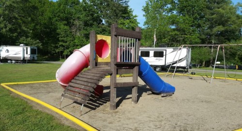 Colorful playground equipment with slides and a climbing structure, set in a grassy area near RVs.