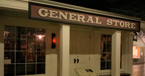 A vintage-style general store with a sign, large windows, and a lantern, set in a dimly lit environment.