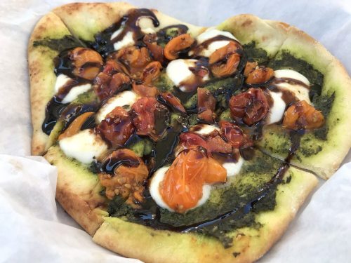 A flatbread topped with pesto, mozzarella, and roasted cherry tomatoes drizzled with balsamic glaze.