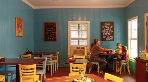 A cozy café with blue walls, featuring tables and chairs, where a woman and two children enjoy coffee and snacks.