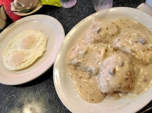 A plate of biscuits smothered in creamy gravy next to a plate with two fried eggs.
