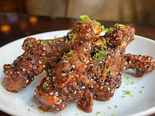 A close-up of glazed chicken wings topped with sesame seeds and green herbs on a white plate.