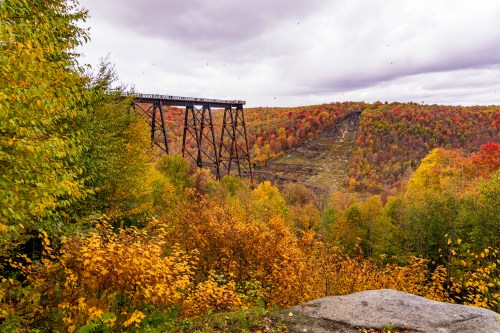 A scenic view of a bridge over a colorful autumn landscape with vibrant trees and a distant hillside.