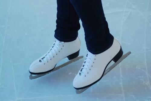 A close-up of a person's feet wearing white ice skates on an ice rink.