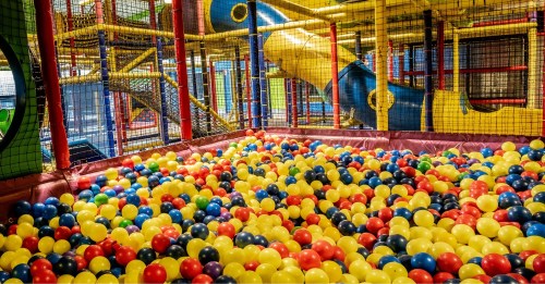 A colorful ball pit filled with yellow, red, and blue balls inside a children's play area with slides and climbing structures.