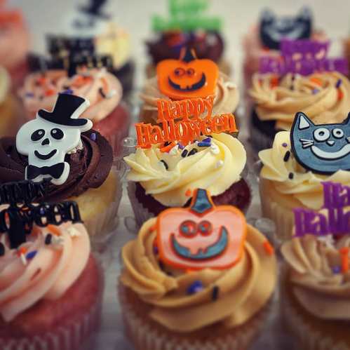 A variety of Halloween-themed cupcakes with colorful frosting and festive decorations, including pumpkins and skeletons.