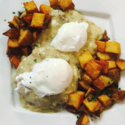 A plate of poached eggs on creamy gravy with seasoned diced potatoes on the side.
