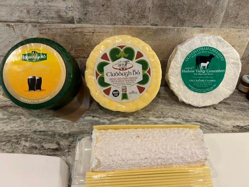 Three types of cheese displayed on a countertop: a round Irish cheese, a yellow cheese with a green design, and a white camembert.