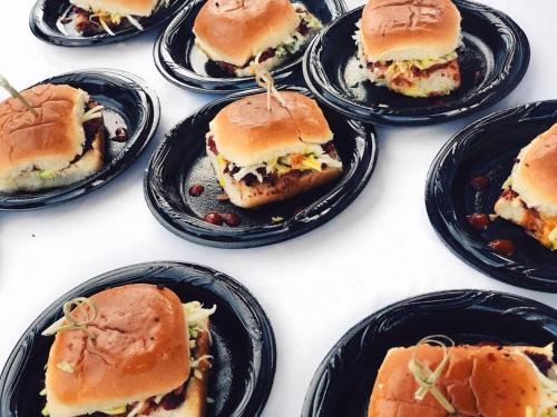 A variety of small sandwiches on black plates, each topped with a toothpick, arranged on a white tablecloth.