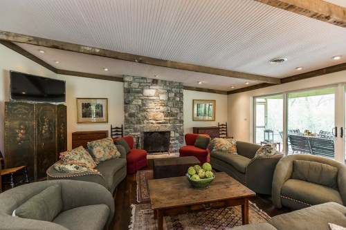 Cozy living room with stone fireplace, comfortable seating, and large windows overlooking a patio.
