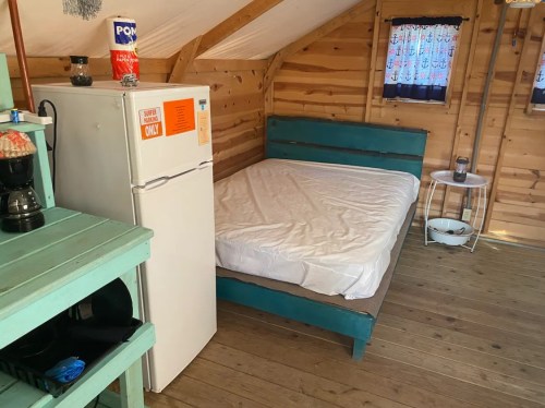 Interior of a cozy cabin featuring a bed, fridge, and wooden decor with a rustic feel.