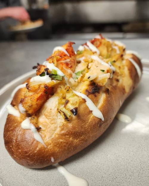 A toasted bun filled with grilled chicken, shrimp, and drizzled with creamy sauce, served on a plate.
