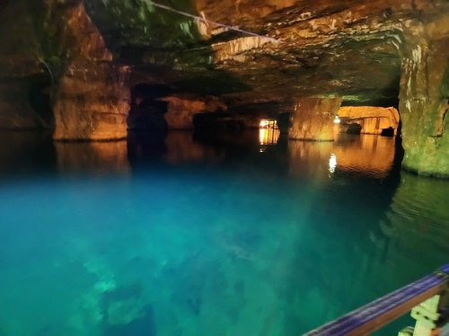 A serene underground cave with calm, clear water reflecting warm lights and rugged stone formations.