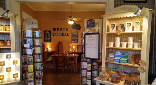 Cozy interior of a kitchen-themed shop with shelves of cookbooks and baking supplies, featuring a warm dining area.
