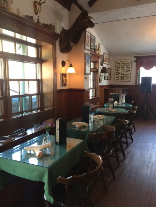 Cozy restaurant interior with wooden tables, green tablecloths, and wall decor featuring mounted animal heads.