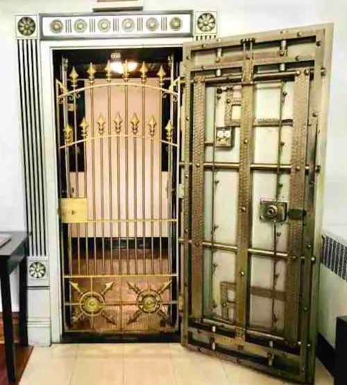 A large, ornate metal vault door with intricate designs, partially open, revealing a glimpse of the interior.