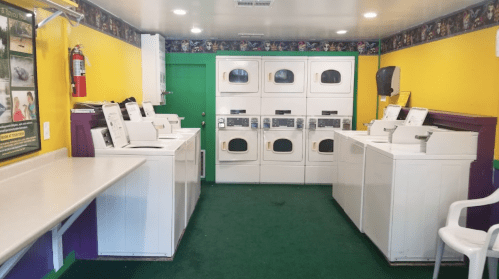A brightly colored laundry room with multiple washing machines and dryers, featuring green carpet and a white chair.