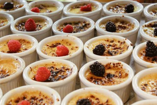 A close-up of individual crème brûlée desserts topped with raspberries and blackberries in white ramekins.