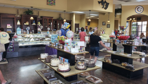 A bustling bakery interior with display cases of cakes, pastries, and customers browsing the treats.