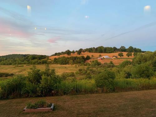 A serene landscape featuring rolling hills, green fields, and a few farm buildings under a pastel sky at dusk.